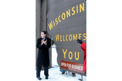 Walker Next to Welcome to Wisconsin Sign